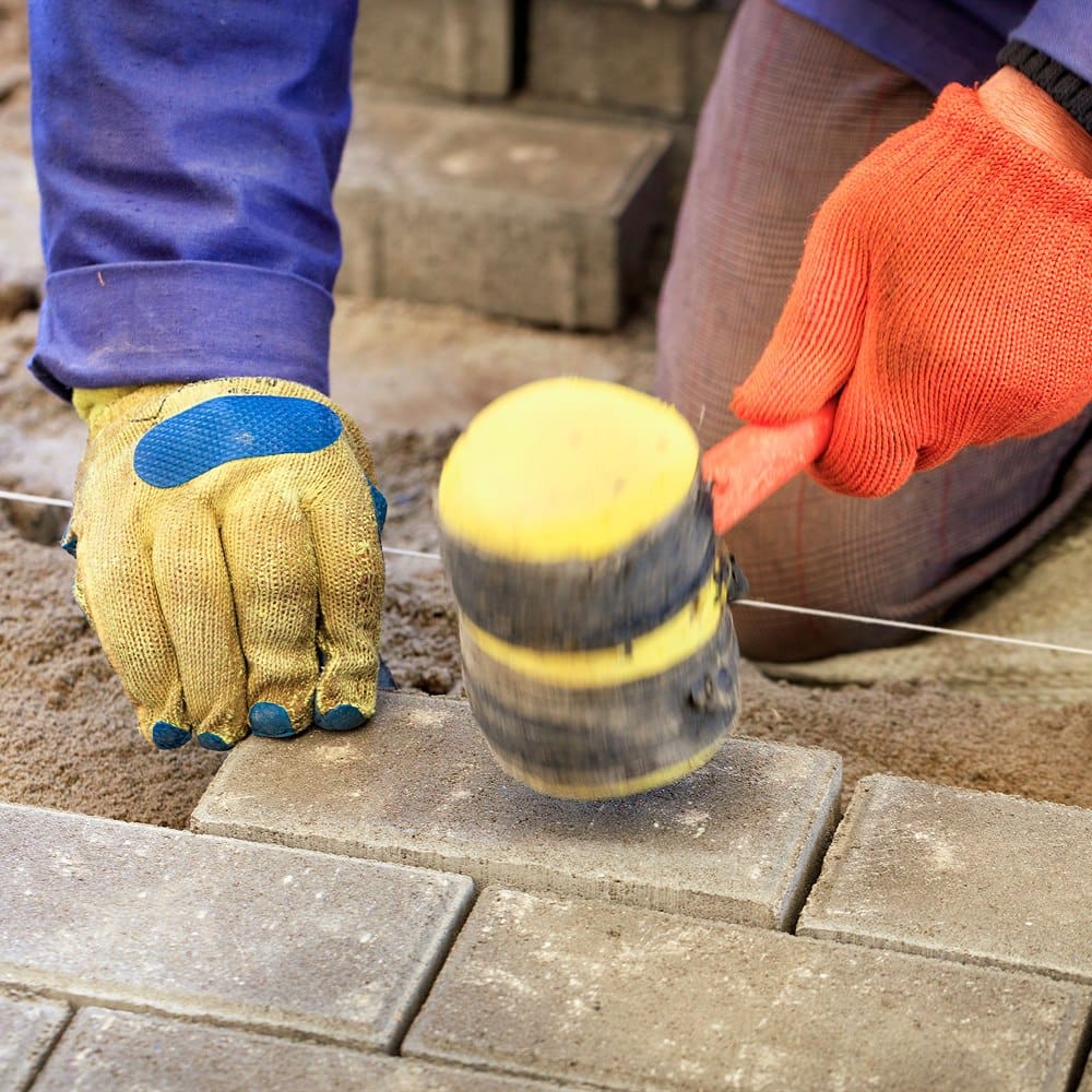 Bricklayer using hammer to lay pavers for patio