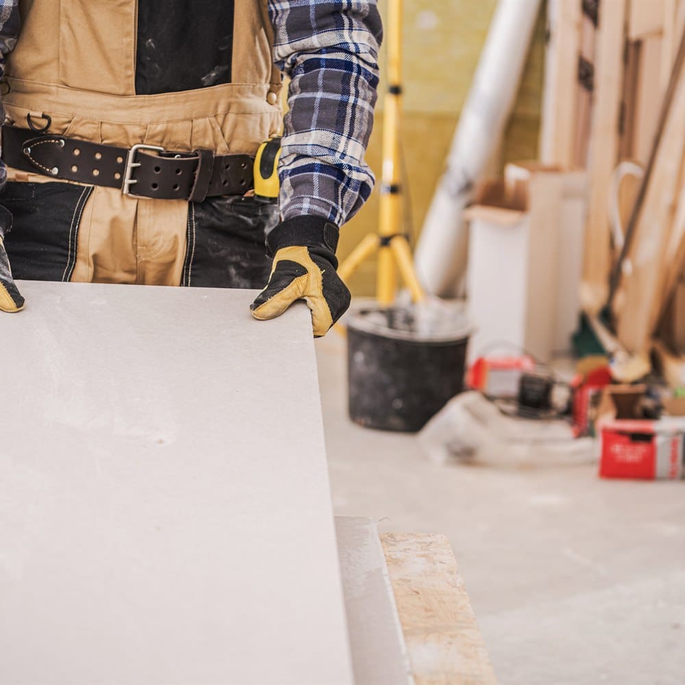 Construction worker carrying sheetrock inside building