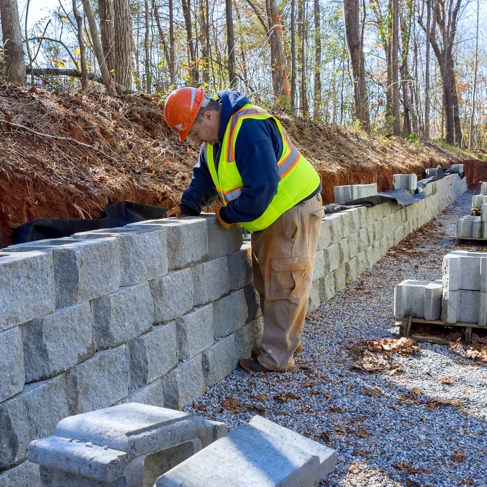 Man building retaining wall with concrete blocks