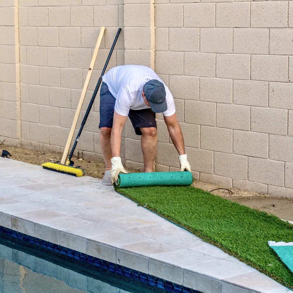 man-unrolling-artificial-turf-near-poolside-in-bac Man unrolling artificial turf near poolside