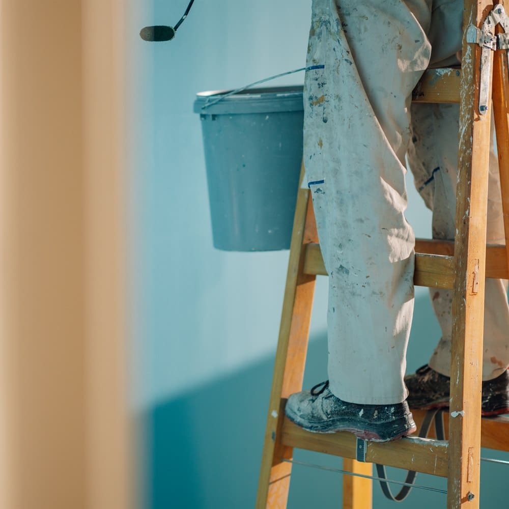 Painter on ladder with paint and paint roller