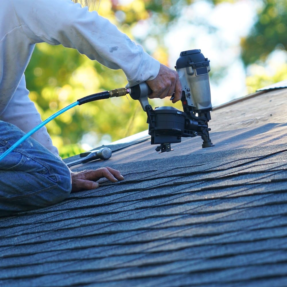 Roofer using nail gun on asphalt shingles